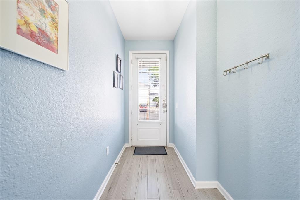 A light blue entryway features wood-look tile flooring, a white door, and wall-mounted coat hooks — 2556 RENSHAW STREET, KISSIMMEE, FL