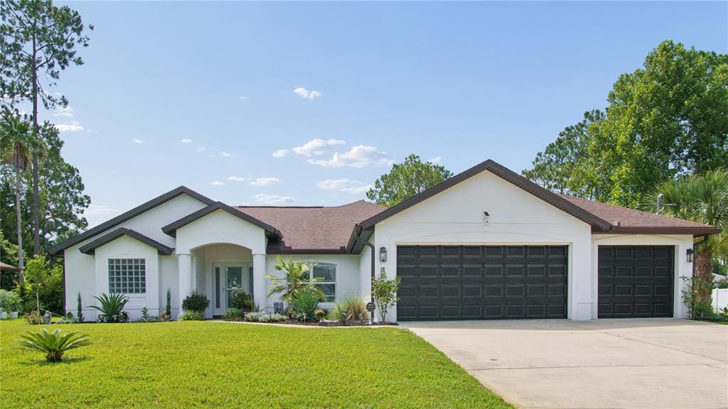 A single-story white house with a brown roof and two black garage doors — 46 BROOKLYN LANE, PALM COAST, FL