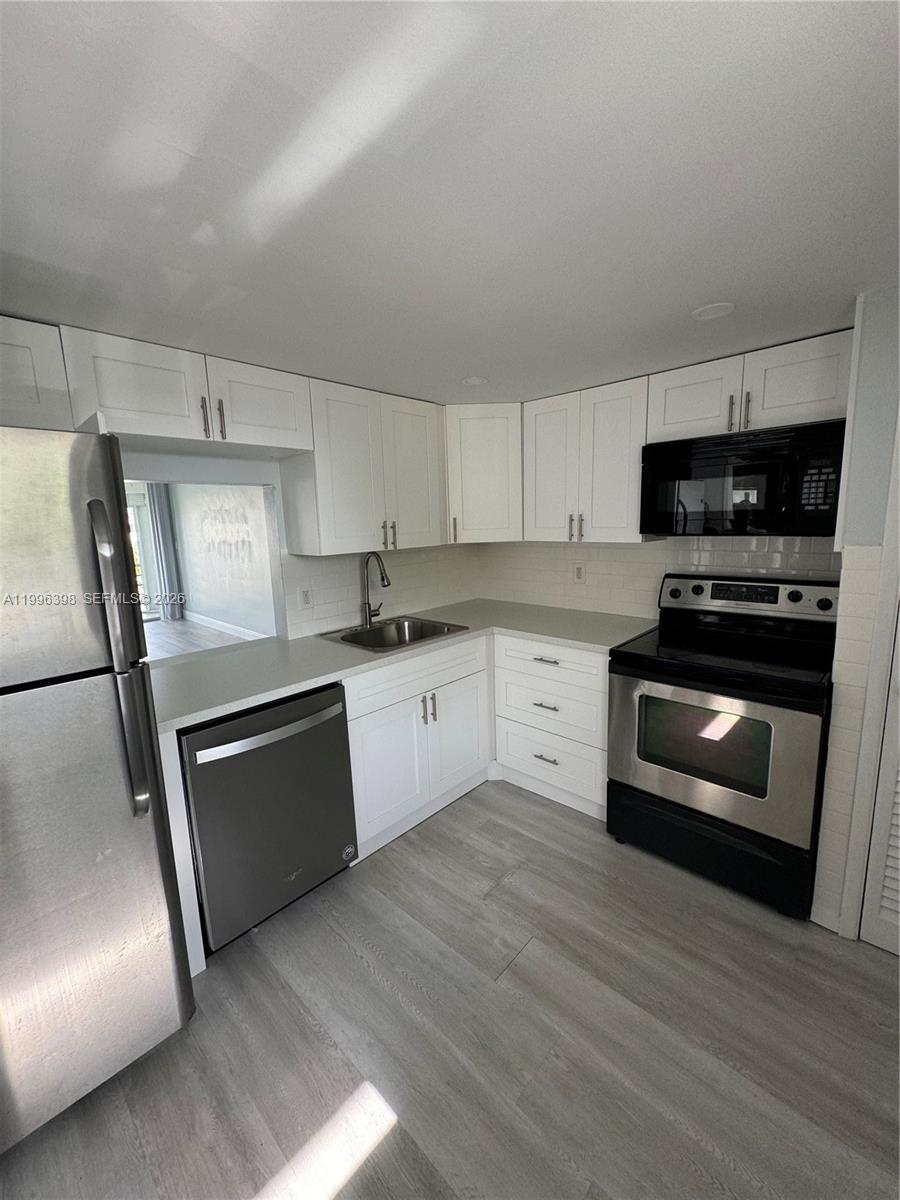 A kitchen features white cabinets, stainless steel appliances, and light-colored wood-look flooring — 1398 NE 191st St # C305, Miami FL 33179, MIAMI, FL