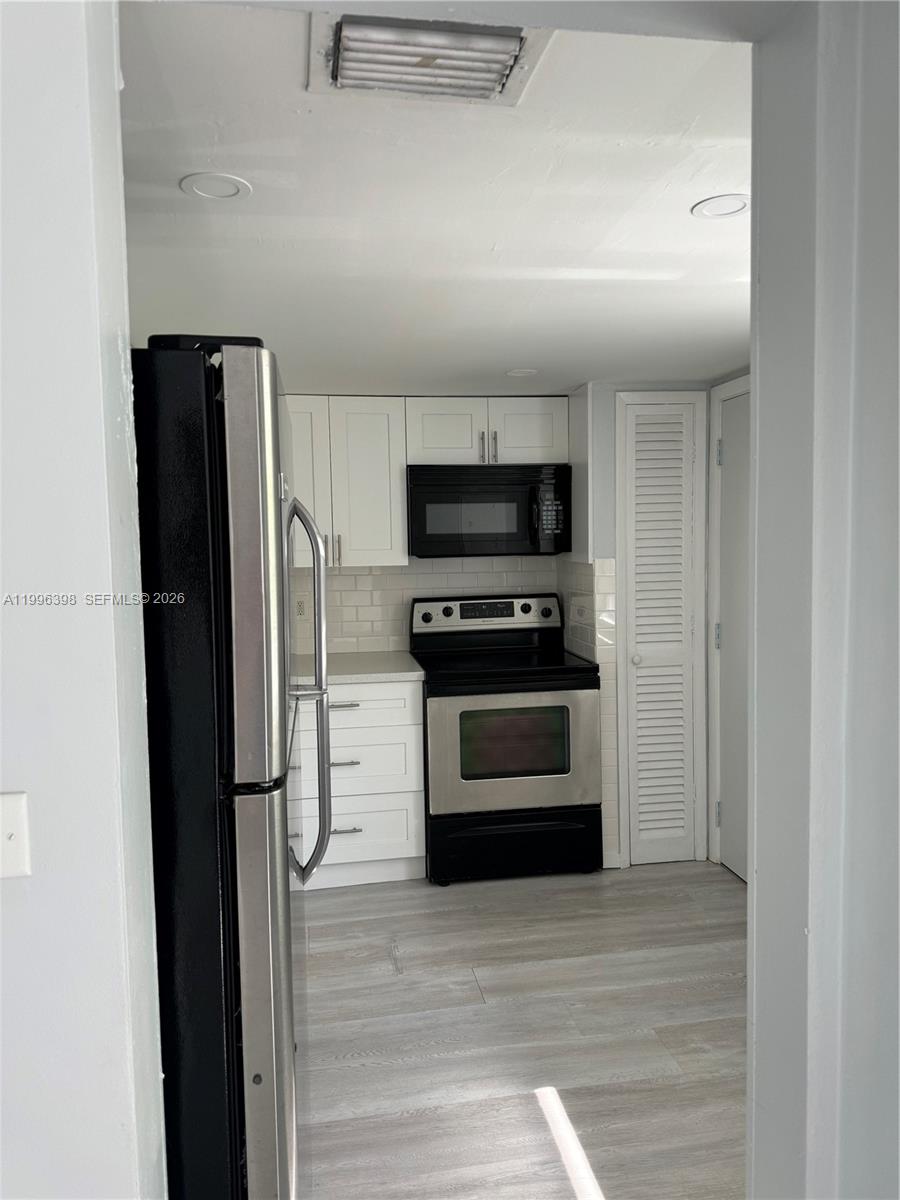A kitchen features white cabinets, stainless steel appliances, and light-colored wood-look flooring — 1398 NE 191st St # C305, Miami FL 33179, MIAMI, FL