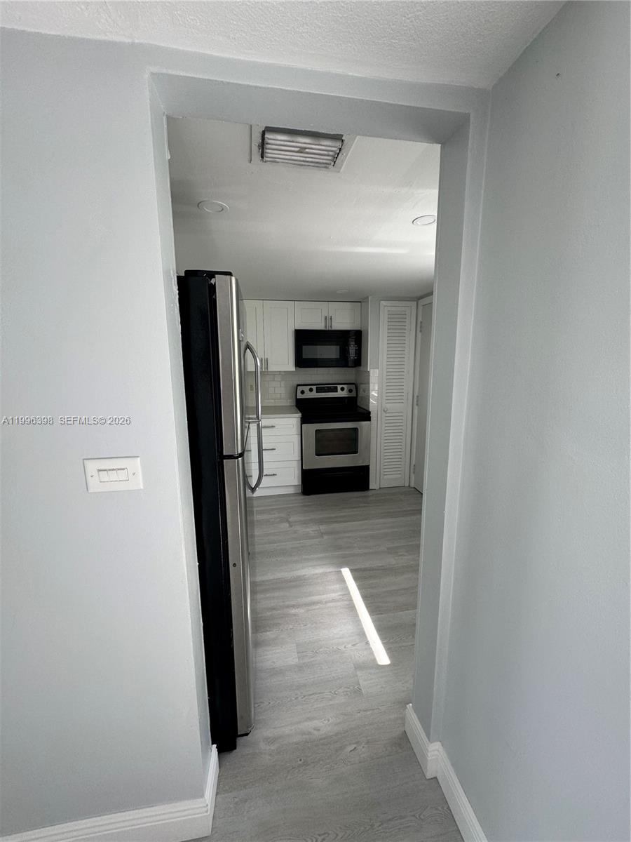 A view through a doorway shows a kitchen with white cabinets and stainless appliances — 1398 NE 191st St # C305, Miami FL 33179, MIAMI, FL