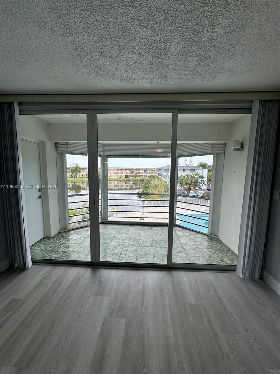 A living room features light wood-look flooring and a sliding glass door leading to a balcony — 1398 NE 191st St # C305, Miami FL 33179, MIAMI, FL
