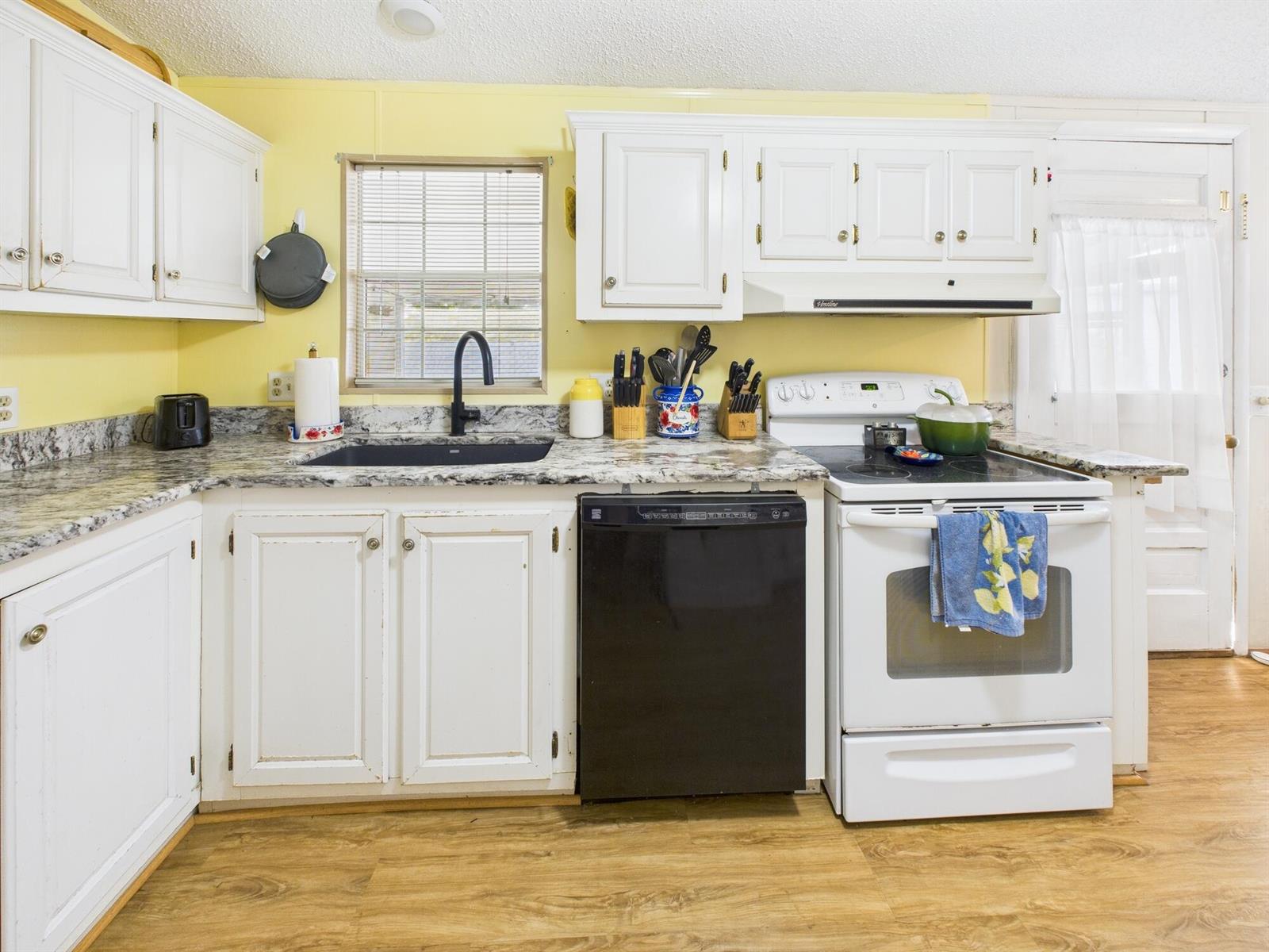 A kitchen features white cabinets, yellow walls, granite countertops, and a mix of appliances — 102 NE 8th Avenue, Okeechobee FL 34972, OKEECHOBEE, FL