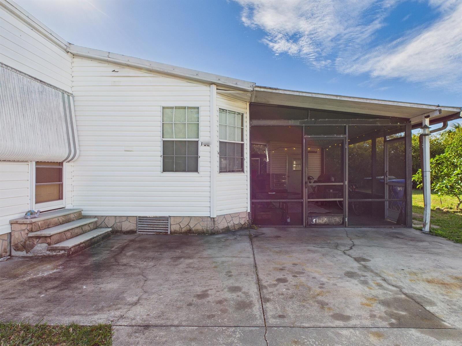 A white mobile home exterior features a concrete patio, stone skirting, and a screened-in porch — 102 NE 8th Avenue, Okeechobee FL 34972, OKEECHOBEE, FL