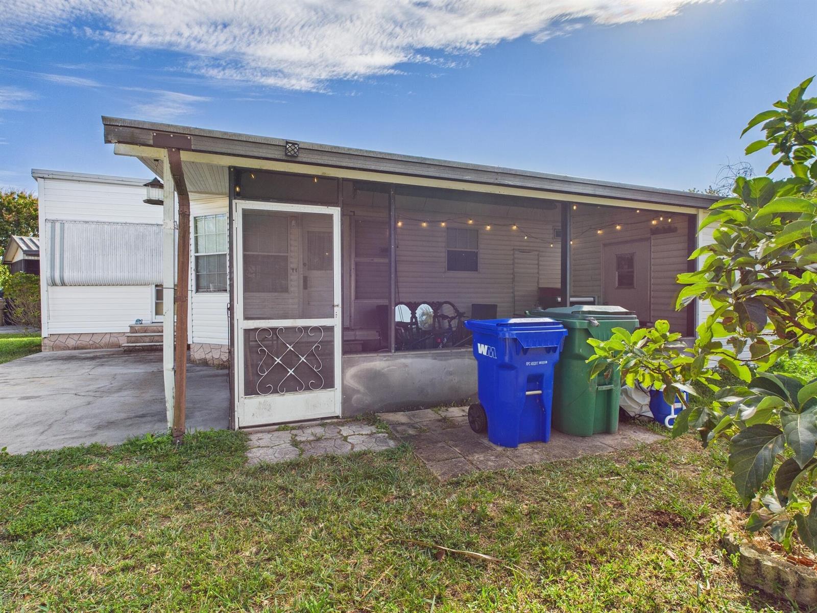 A screened-in porch with a white door sits beside two large trash bins outdoors — 102 NE 8th Avenue, Okeechobee FL 34972, OKEECHOBEE, FL