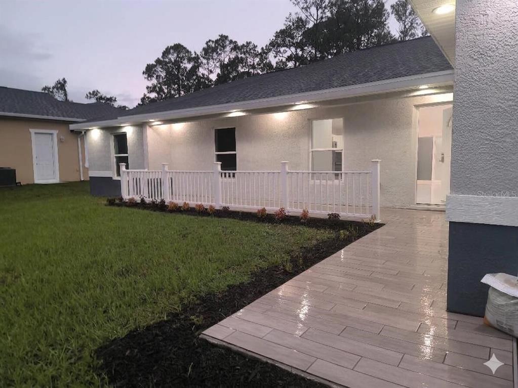 A white house exterior features a tiled patio, a white railing, and a landscaped lawn — 5609 LAKEWOOD ROAD, SEBRING, FL