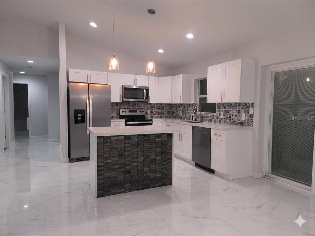 A modern kitchen features white cabinets, stainless steel appliances, a stone-accented island, and marble flooring — 5609 LAKEWOOD ROAD, SEBRING, FL