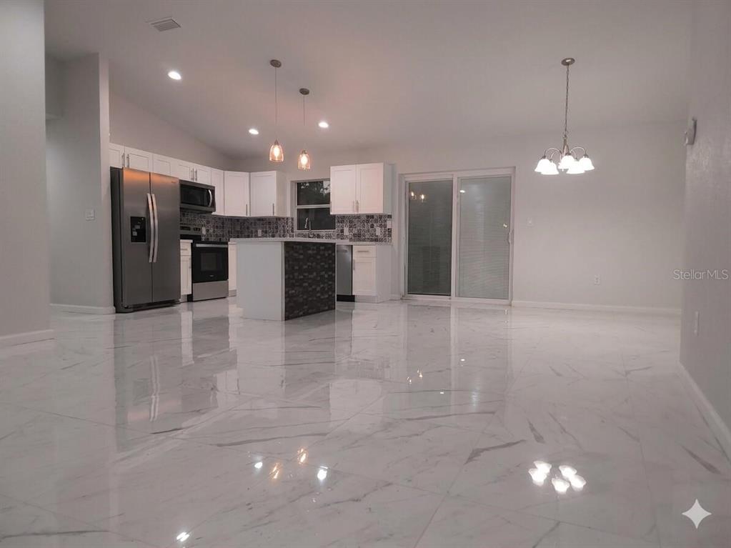 A modern kitchen with white cabinets, stainless steel appliances, and polished marble-look tile flooring — 5609 LAKEWOOD ROAD, SEBRING, FL