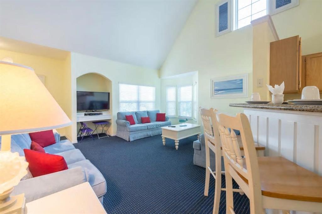 A living room with blue sofas, red pillows, a vaulted ceiling, and a breakfast bar — 3013 BONFIRE BEACH DRIVE UNIT 201, KISSIMMEE, FL