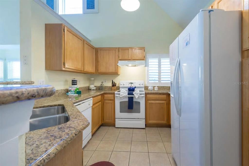 A kitchen features light wood cabinets, granite countertops, white appliances, and a vaulted ceiling — 3013 BONFIRE BEACH DRIVE UNIT 201, KISSIMMEE, FL