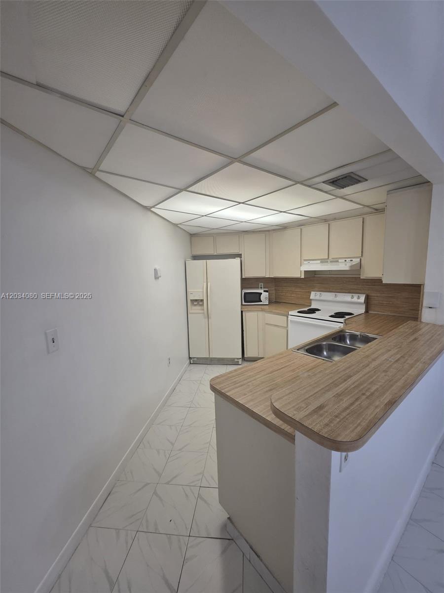 This kitchen features white cabinets, laminate countertops, a drop ceiling, and white tile flooring — 9429 Fontainebleau Blvd # 33, Miami FL 33172, MIAMI, FL
