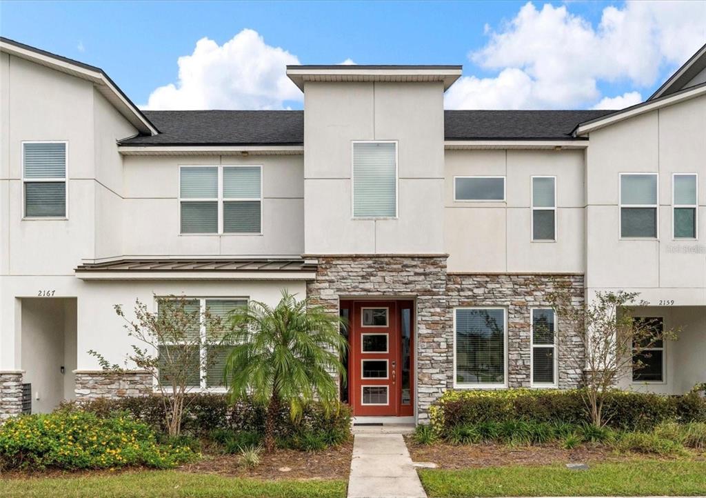 A two-story townhouse exterior features white siding, stone accents, and a red front door — 2163 COPPER BELL PLACE, KISSIMMEE, FL