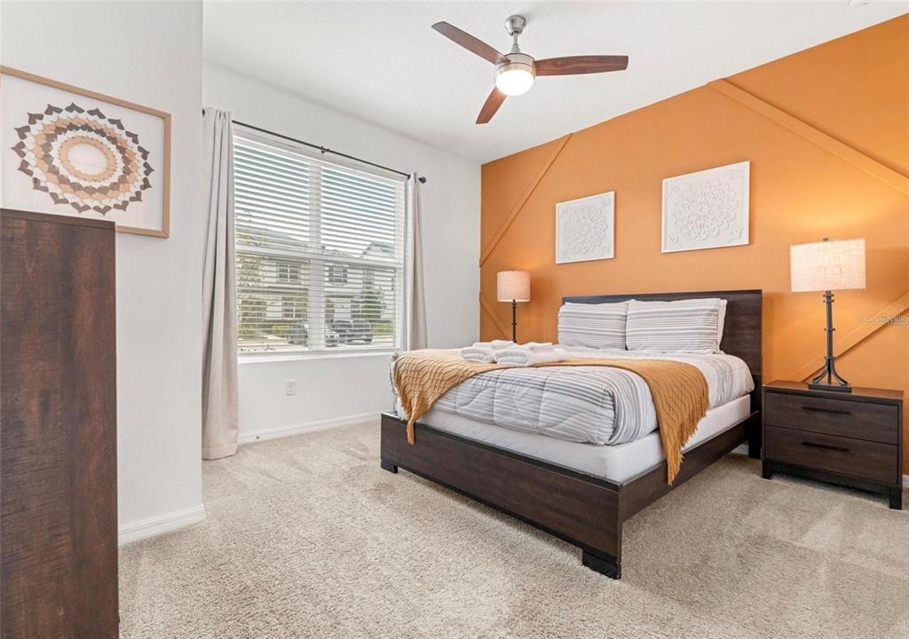 A bedroom features a bed with striped bedding, an orange accent wall, and a ceiling fan — 2163 COPPER BELL PLACE, KISSIMMEE, FL