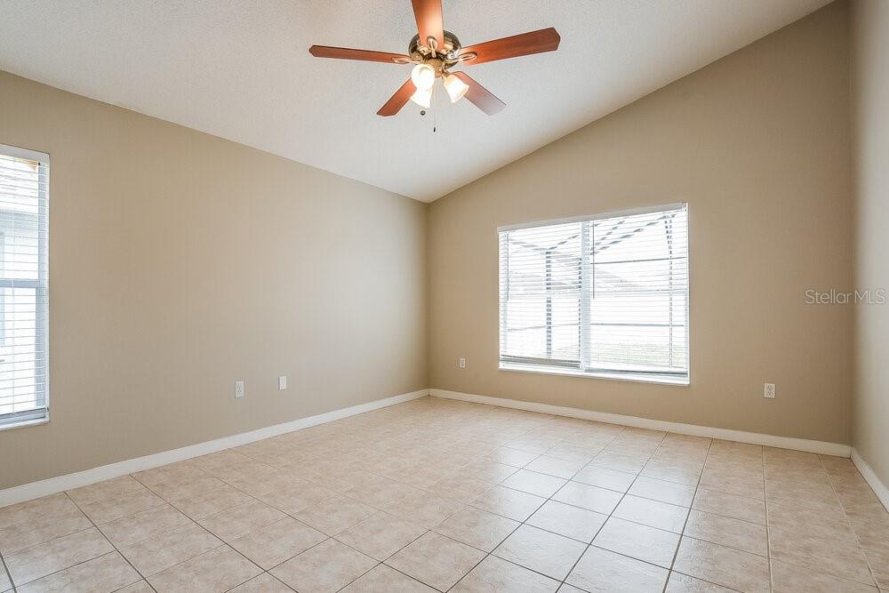 An empty room with beige walls, tile flooring, a ceiling fan, and two windows — 4616 FALCON AVENUE, KISSIMMEE, FL