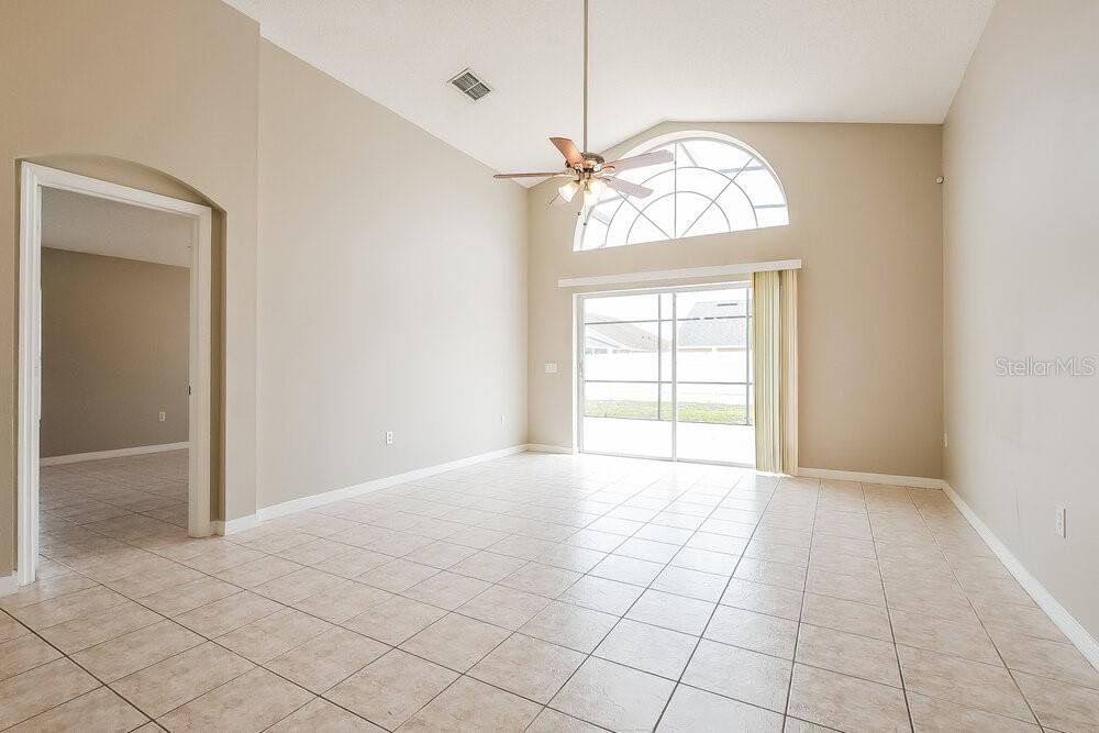 A living room with vaulted ceilings, tile flooring, a ceiling fan, and sliding glass doors — 4616 FALCON AVENUE, KISSIMMEE, FL