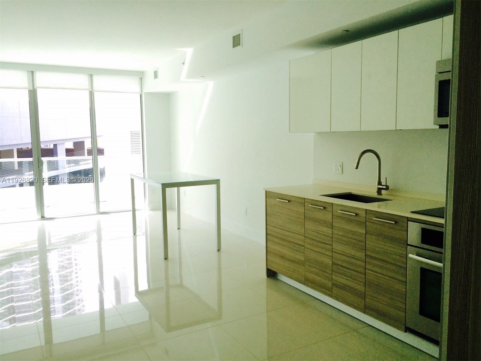 A modern kitchen features wood-grain lower cabinets, white upper cabinets, and a glass dining table — 1300 BRICKELL BAY DR # 1100, Miami FL 33131, MIAMI, FL