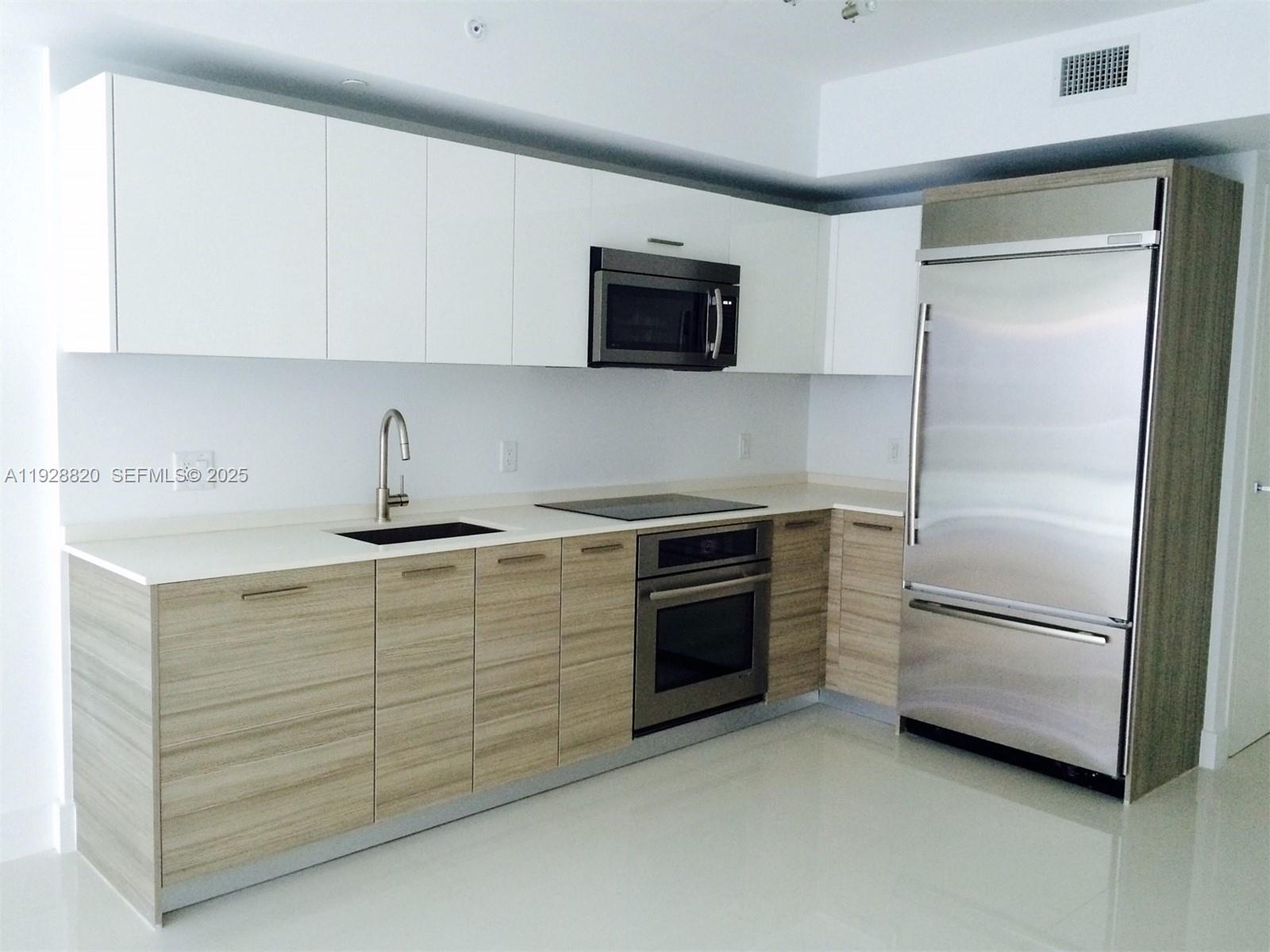 A modern kitchen features white upper cabinets, wood-grain lower cabinets, and stainless steel appliances — 1300 BRICKELL BAY DR # 1100, Miami FL 33131, MIAMI, FL