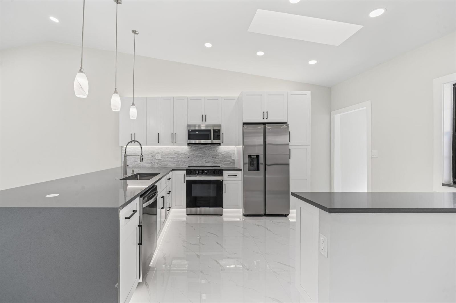 A modern kitchen features white cabinets, stainless steel appliances, gray countertops, and white tile flooring — 6371 Kings Gate Circle, Delray Beach FL 33484, DELRAY BEACH, FL