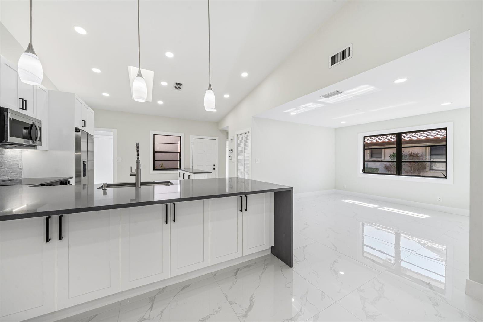 A modern kitchen with white cabinets, a dark island countertop, and white marble-look flooring — 6371 Kings Gate Circle, Delray Beach FL 33484, DELRAY BEACH, FL
