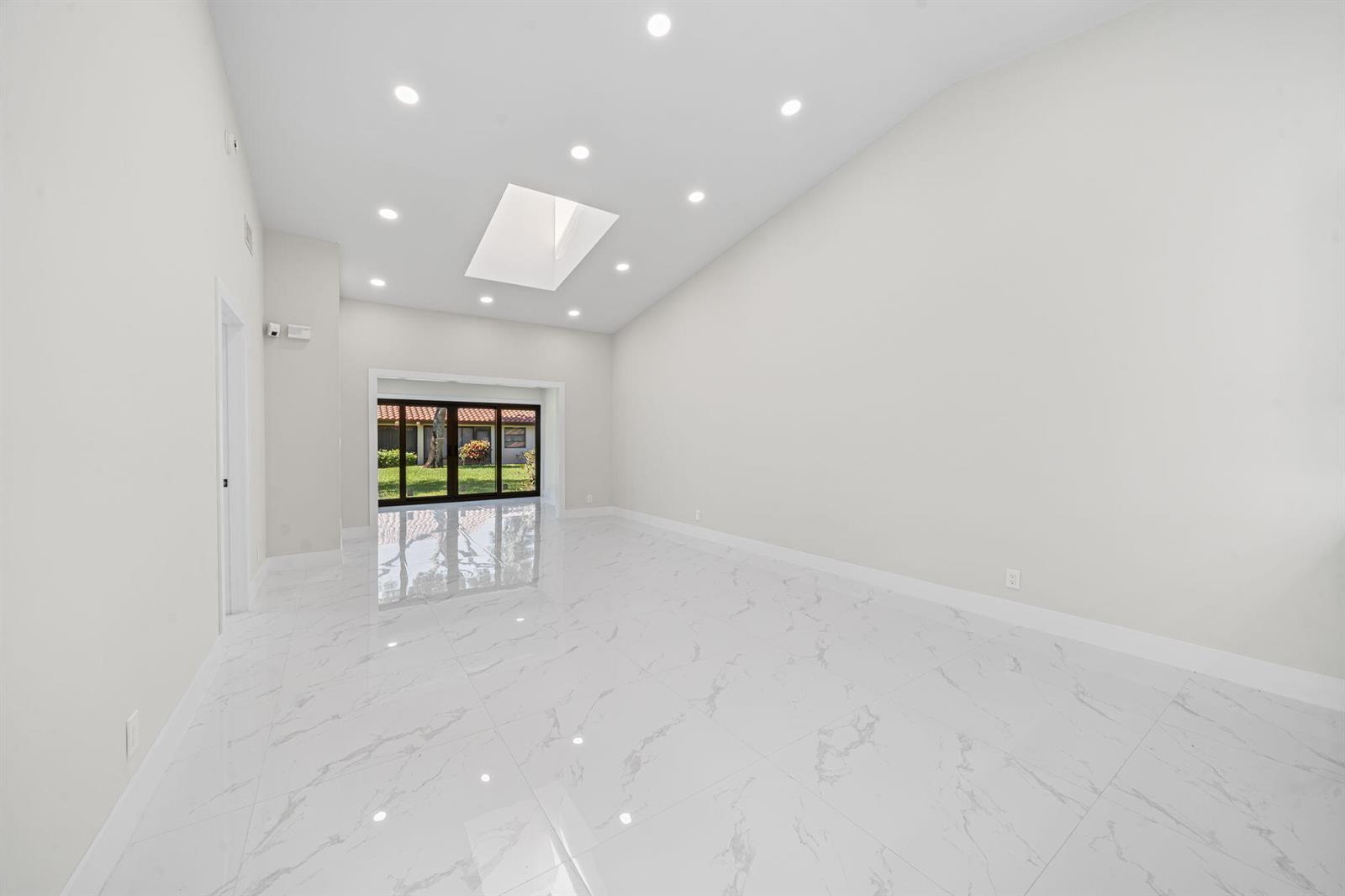 An empty room with white marble floors, recessed lighting, a skylight, and glass sliding doors — 6371 Kings Gate Circle, Delray Beach FL 33484, DELRAY BEACH, FL