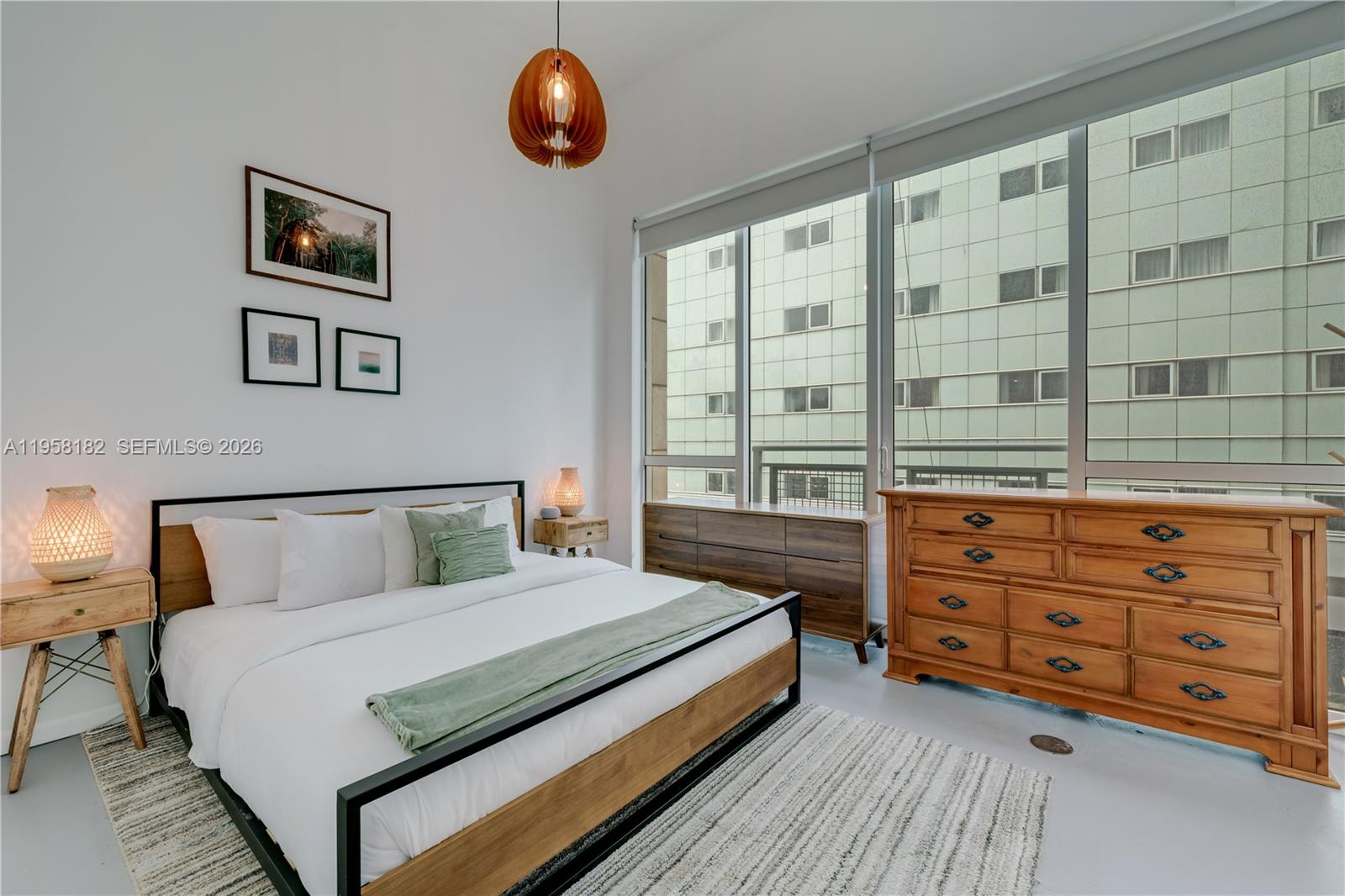 A bedroom features a bed with a metal frame, wooden furniture, and large floor-to-ceiling windows — 253 NE 2nd St # 228, Miami FL 33132, MIAMI, FL