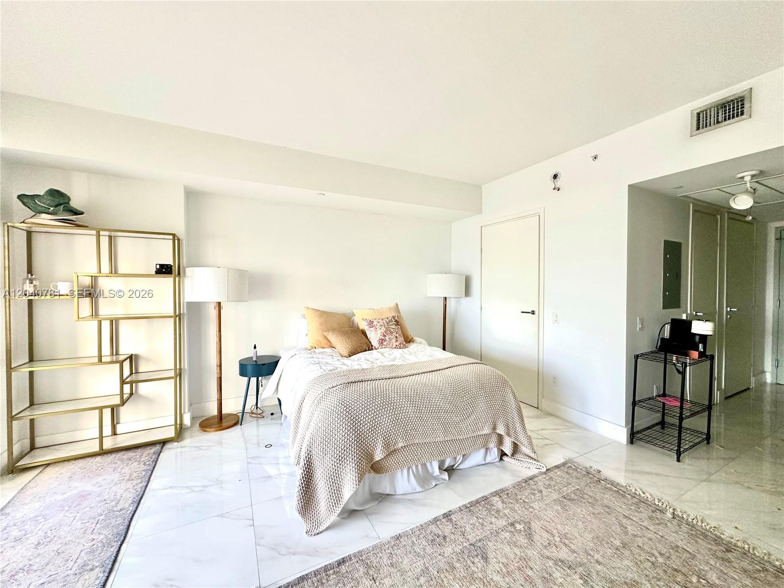 A bedroom features a bed, two floor lamps, a gold shelving unit, and marble flooring — 1300 Brickell Bay Dr # 2106, Miami FL 33131, MIAMI, FL