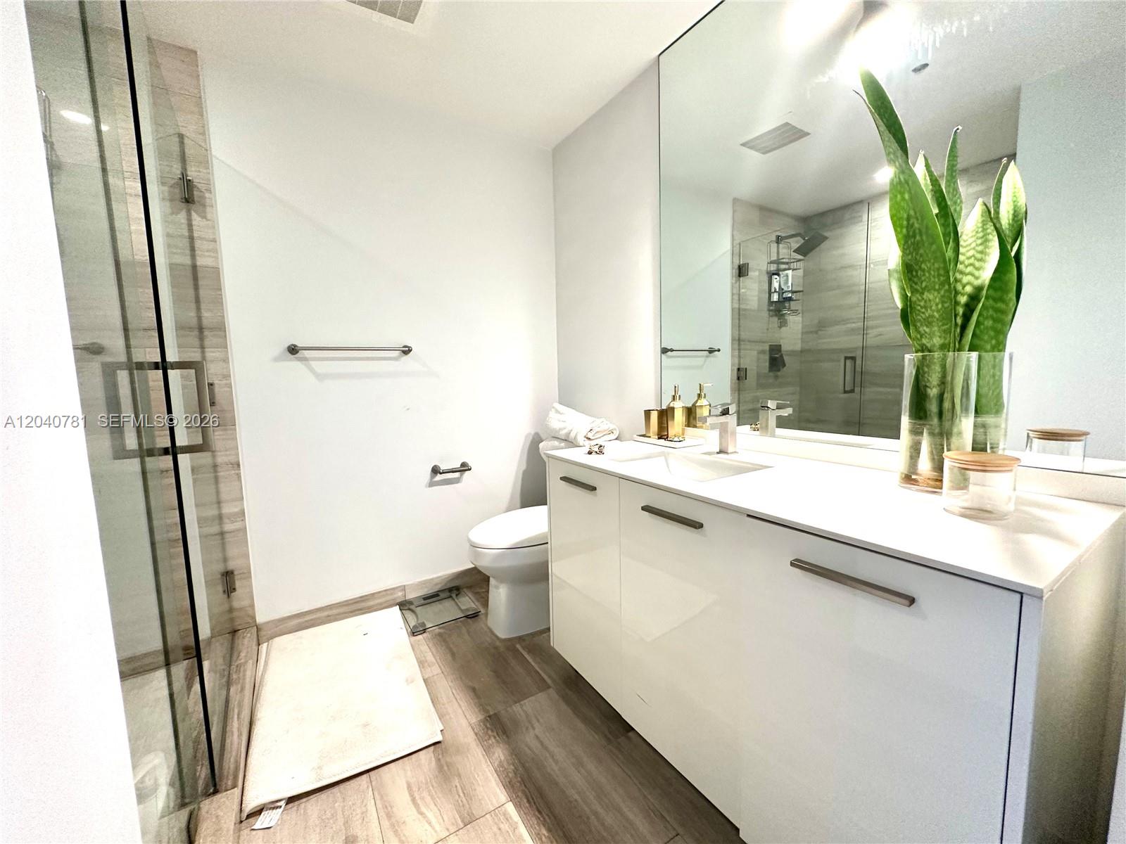 A modern bathroom features a glass-enclosed shower, a white vanity, and wood-look tile flooring — 1300 Brickell Bay Dr # 2106, Miami FL 33131, MIAMI, FL