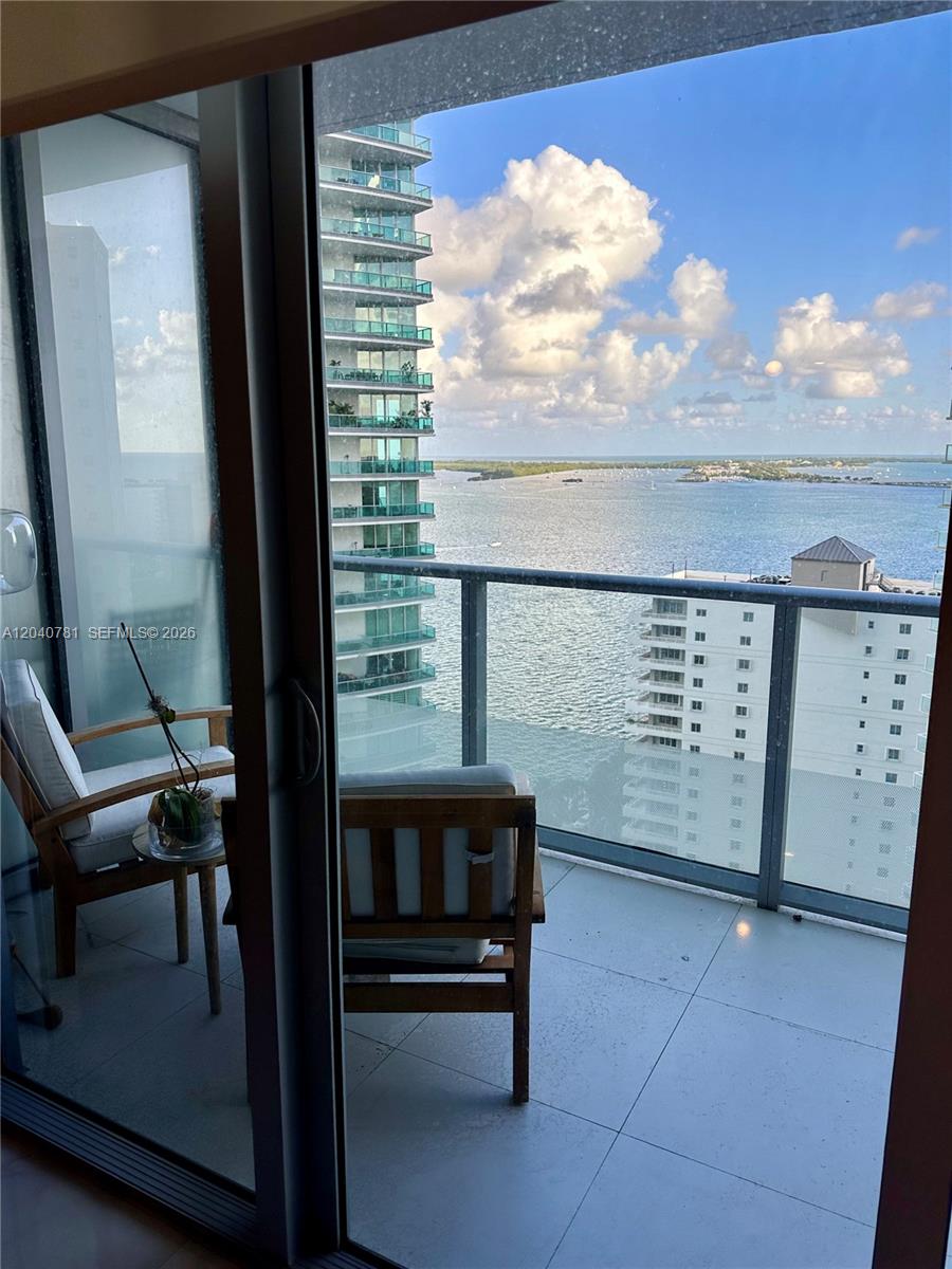 A balcony with two wooden chairs overlooks a bay and neighboring high-rise buildings — 1300 Brickell Bay Dr # 2106, Miami FL 33131, MIAMI, FL
