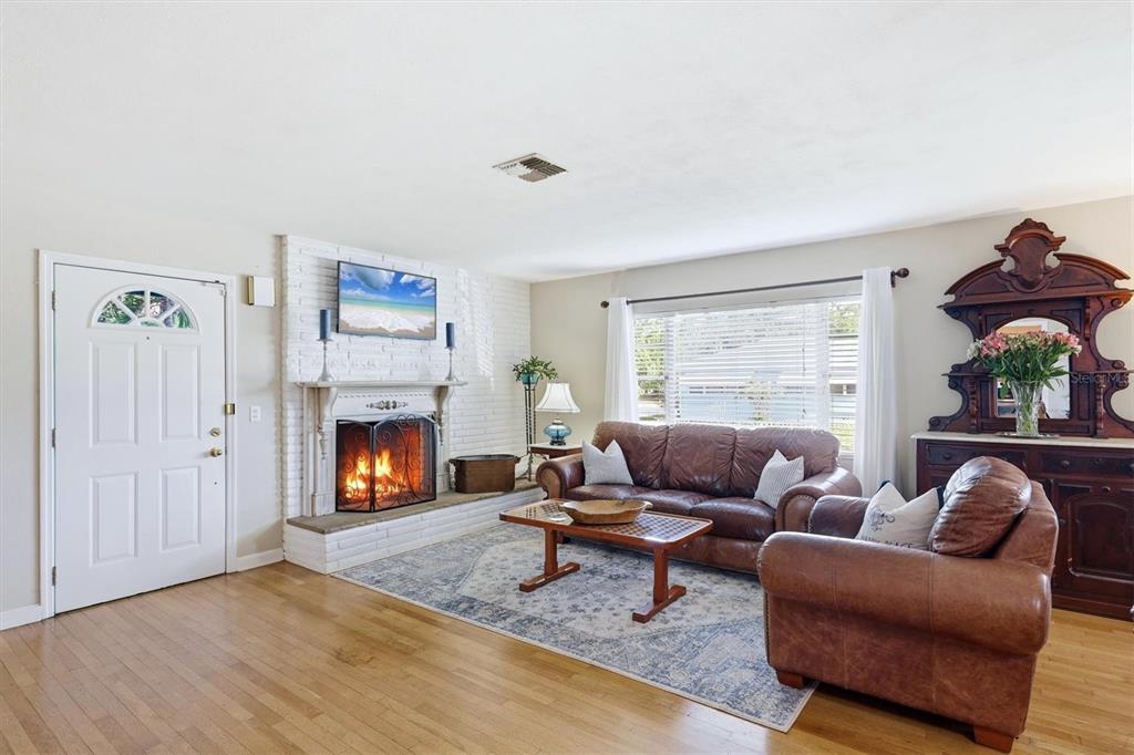 A living room features a white brick fireplace, hardwood floors, and brown leather furniture — 401 28TH STREET W, BRADENTON, FL