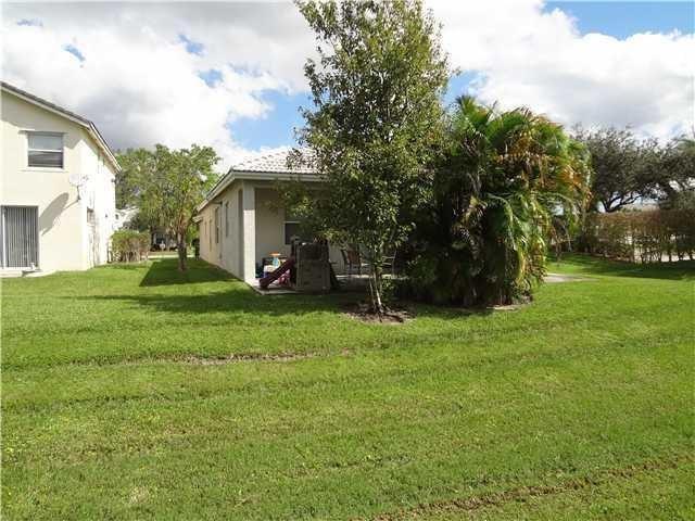 A view of a house exterior with a covered patio, lawn, and landscaping — 7953 NW 70th Avenue, Parkland FL 33067, PARKLAND, FL