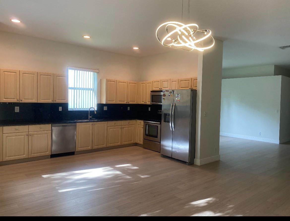 A kitchen features light wood cabinets, black countertops, stainless steel appliances, and a modern chandelier — 7953 NW 70th Avenue, Parkland FL 33067, PARKLAND, FL
