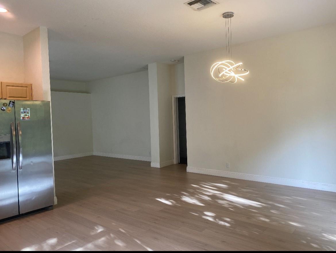 A kitchen and dining area featuring light wood flooring, a stainless steel refrigerator, and a chandelier — 7953 NW 70th Avenue, Parkland FL 33067, PARKLAND, FL