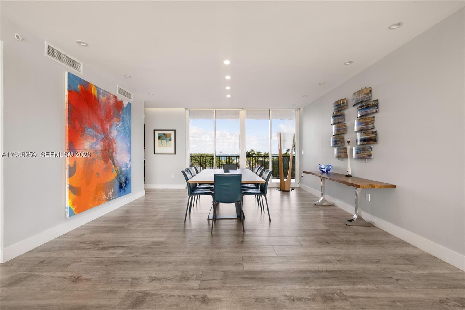 A dining room features a large abstract painting, a long wooden table, and floor-to-ceiling windows — 1000 Venetian Way # 502, Miami FL 33139, MIAMI, FL