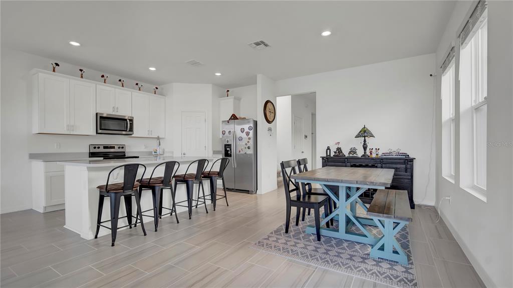 A kitchen with white cabinets and an island opens to a dining area with bench seating — 4704 HOMESTEAD TRAIL, ST CLOUD, FL