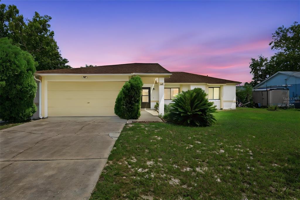 A single-story house with a beige exterior, a two-car garage, and a concrete driveway — 1418 CATALINA BOULEVARD, DELTONA, FL