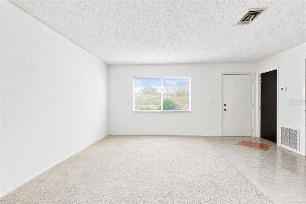 A living room with beige carpet, white walls, a window, and a tiled entryway — 1418 CATALINA BOULEVARD, DELTONA, FL