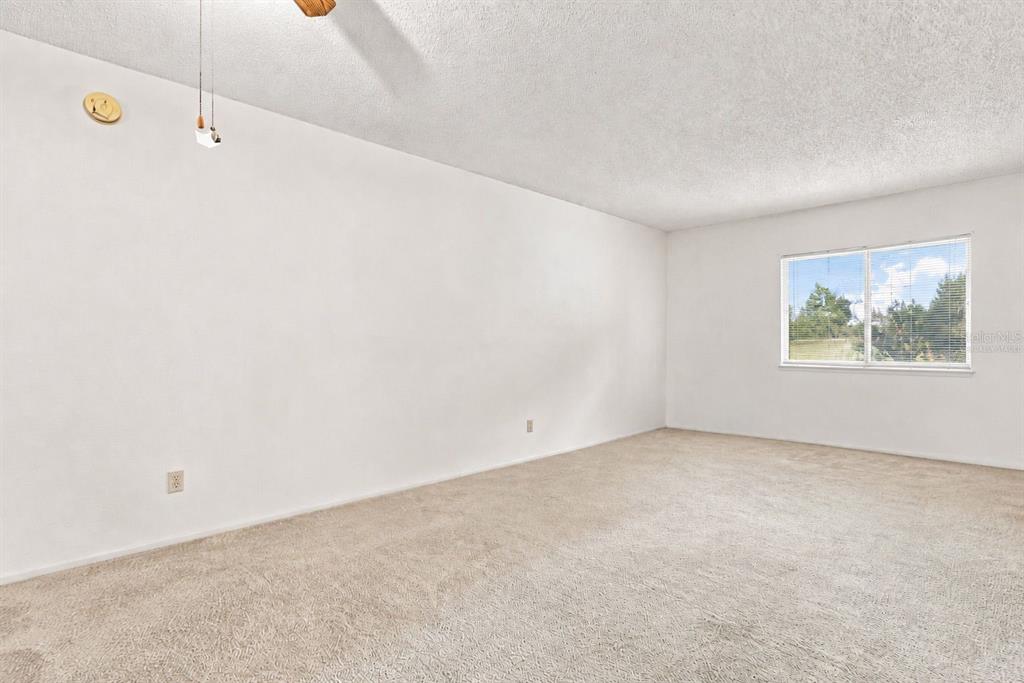 An empty room features white walls, beige carpeting, a ceiling fan, and a single window — 1418 CATALINA BOULEVARD, DELTONA, FL