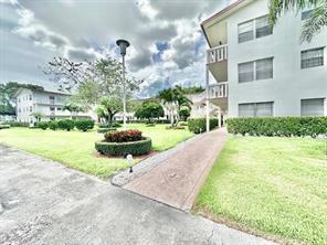 A paved walkway leads through a grassy courtyard between two multi-story apartment buildings — 390 Fanshaw J, Boca Raton FL 33434, BOCA RATON, FL