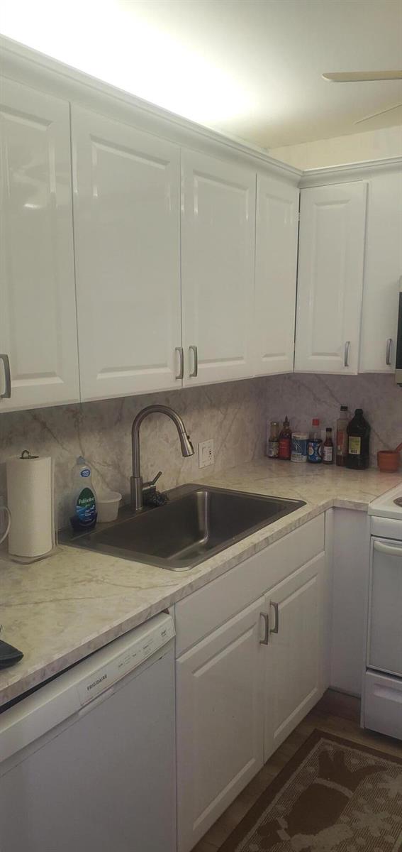 A kitchen features white cabinets, a stainless steel sink, and a marble-patterned countertop — 390 Fanshaw J, Boca Raton FL 33434, BOCA RATON, FL