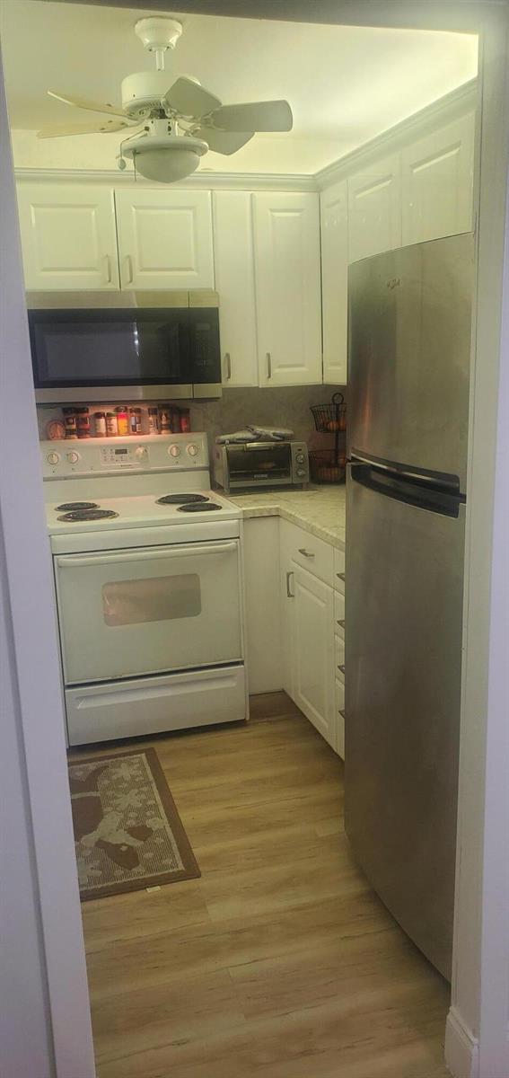 A small kitchen features white cabinets, stainless steel appliances, and light-colored wood-look flooring — 390 Fanshaw J, Boca Raton FL 33434, BOCA RATON, FL