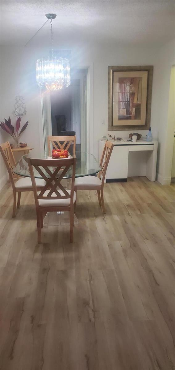 A dining area features a glass-topped table, wooden chairs, a crystal chandelier, and light wood flooring — 390 Fanshaw J, Boca Raton FL 33434, BOCA RATON, FL