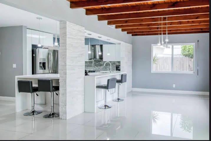 A modern kitchen features white cabinets, a stone-accented island, bar stools, and exposed wood beams — 1905 N 45th Avenue, Hollywood FL 33021, HOLLYWOOD, FL