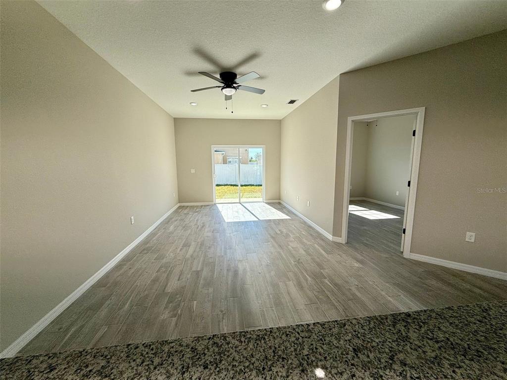 An open living area features wood-look tile flooring, a ceiling fan, and sliding glass doors — 701 CAMEL COURT, POINCIANA, FL