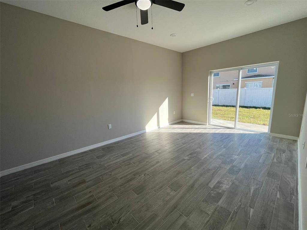An empty room features gray wood-look tile flooring, a ceiling fan, and sliding glass doors — 701 CAMEL COURT, POINCIANA, FL
