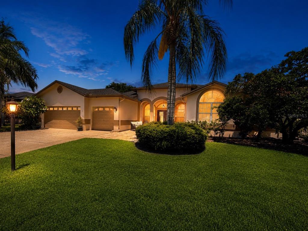 A single-story house with a three-car garage, palm tree, and manicured lawn at dusk — 2093 SWAN LANE, PALM HARBOR, FL