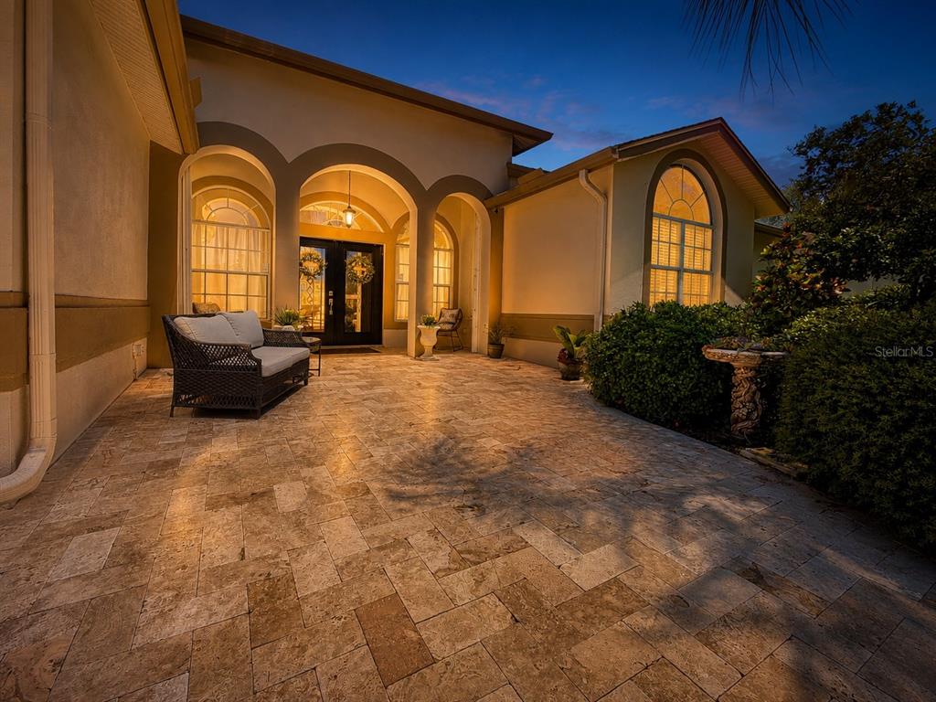 A stone-paved patio features a wicker sofa and arched entryways in front of a house — 2093 SWAN LANE, PALM HARBOR, FL