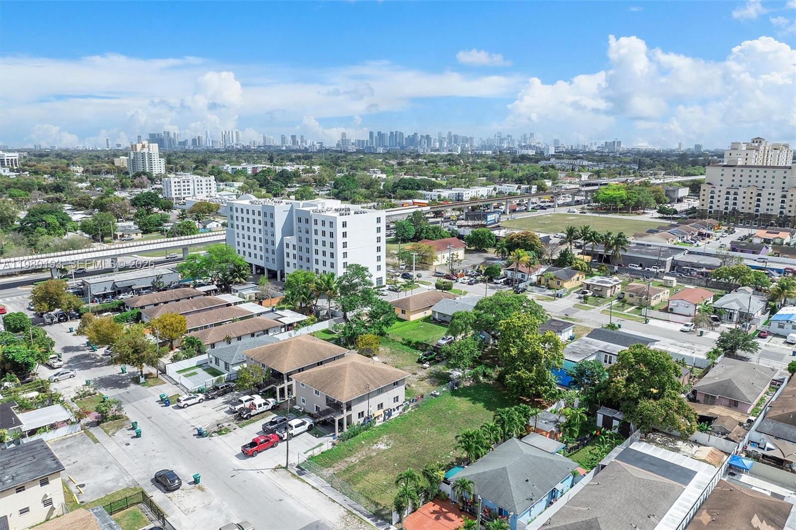 An aerial view shows a residential neighborhood with houses, a large apartment building, and city skyline — 2780 NW 56th St, Miami FL 33142, MIAMI, FL