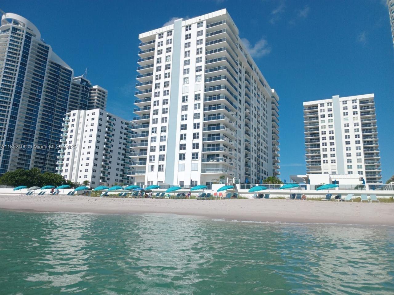 A beach with blue umbrellas in front of several tall white residential buildings — 2751 S Ocean Dr, Hollywood FL 33019, HOLLYWOOD, FL