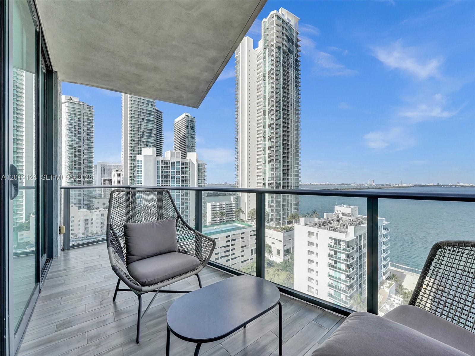 A balcony with two chairs and a table overlooks a city skyline and water — 460 NE 28th St # 1701, Miami FL 33137, MIAMI, FL