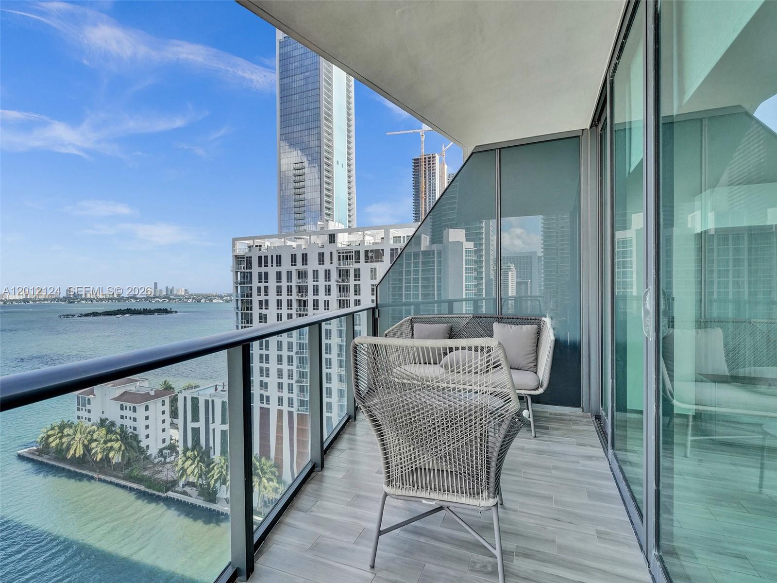 A balcony with outdoor furniture overlooks a bay, nearby buildings, and a construction crane — 460 NE 28th St # 1701, Miami FL 33137, MIAMI, FL